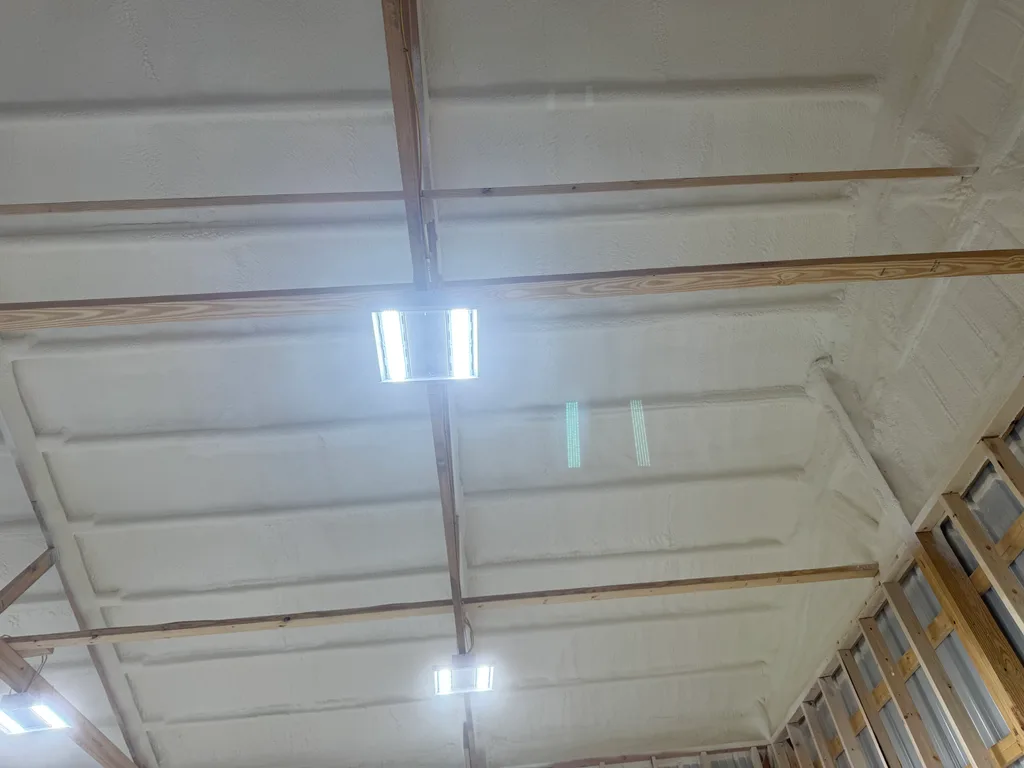 Smooth white foam covering a barn roof deck with a dark timber beam across the span