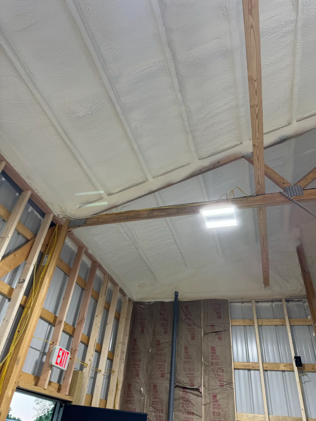 Foamed gable ceiling above steel wall panels with a red exit sign glowing below