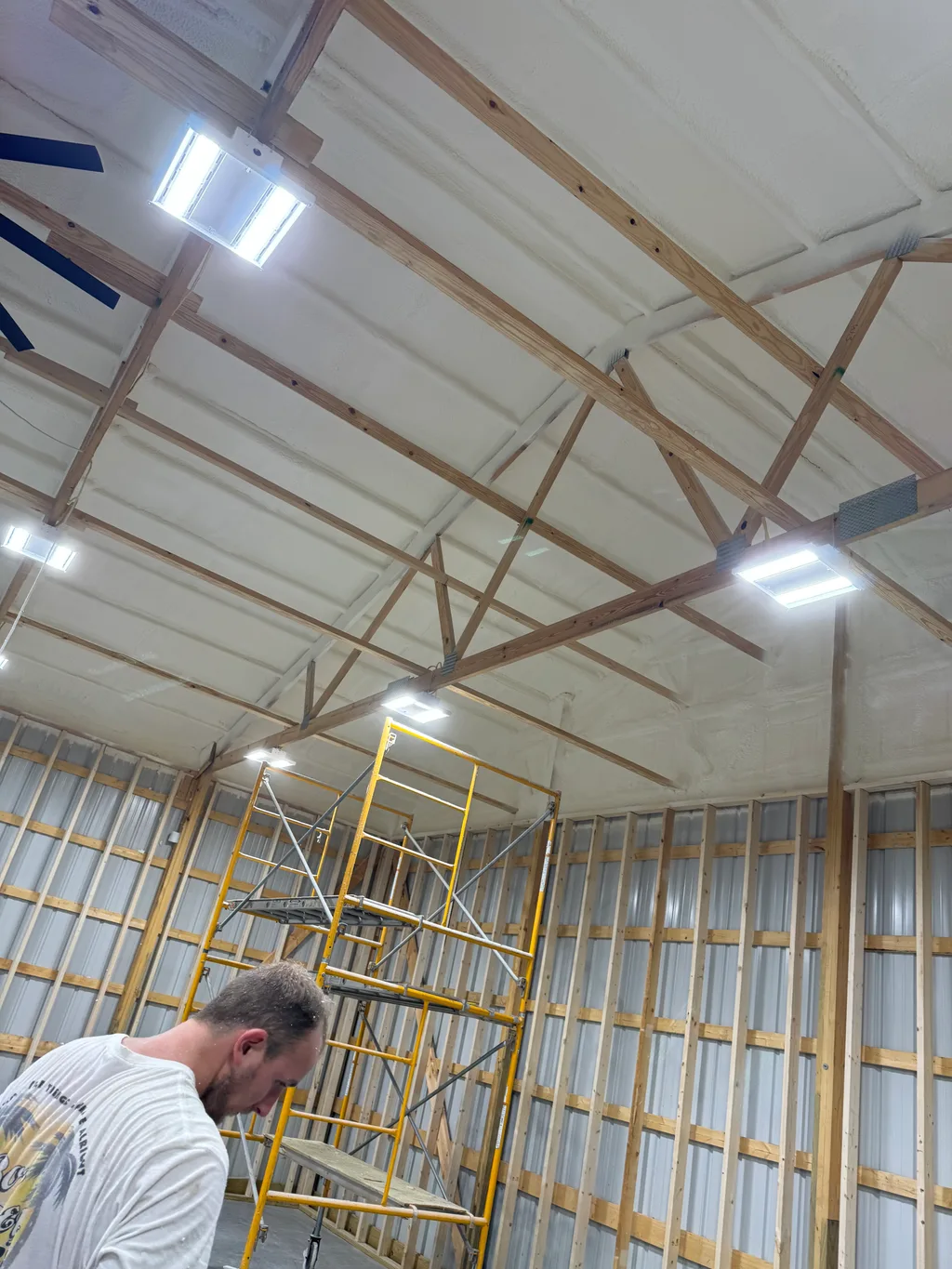 Worker in a white shirt beside yellow rolling scaffold under a freshly foamed ceiling