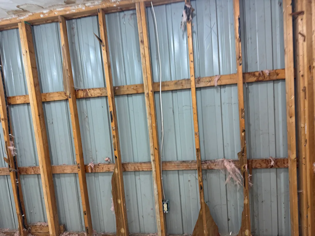 Bare timber studs against unfinished steel wall panels before any insulation is applied
