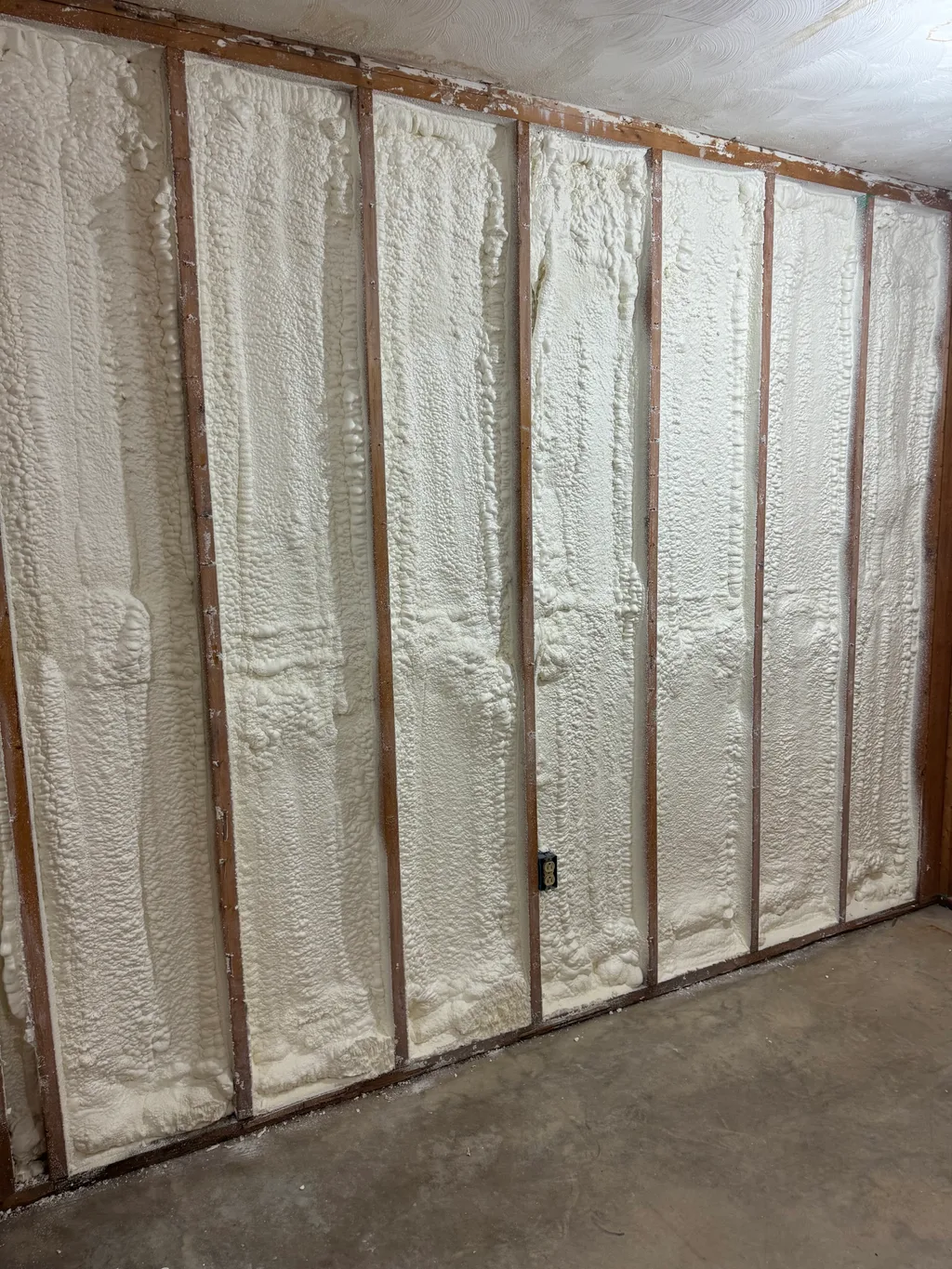 Cream foam filling every stud bay of a wall above a bare concrete floor