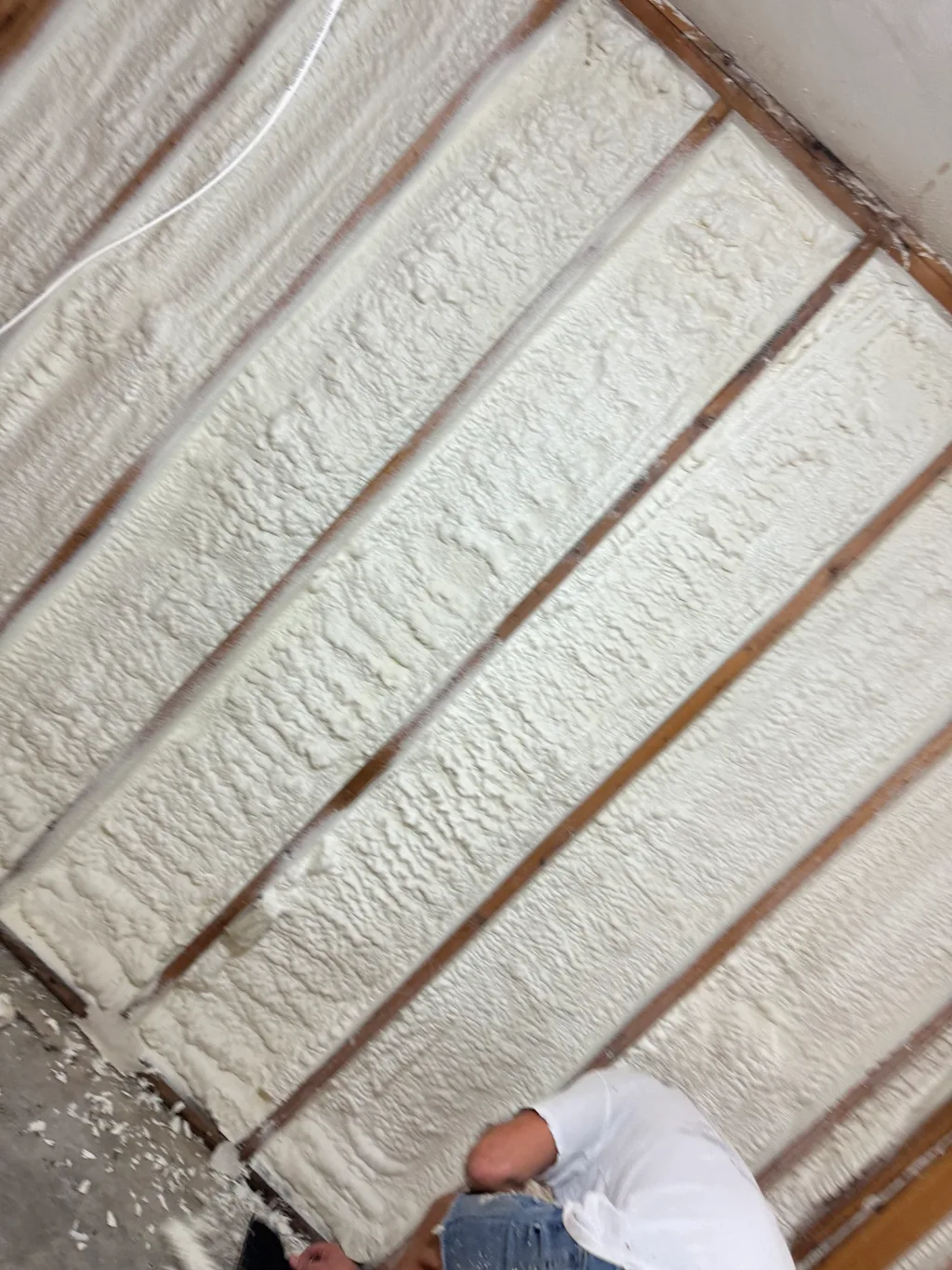 Worker kneeling in a white shirt below a sloping ceiling filled with cream foam