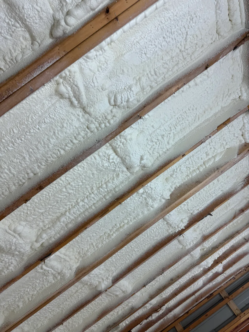 Close view of rough cream foam filling narrow rafter bays up to the timber face