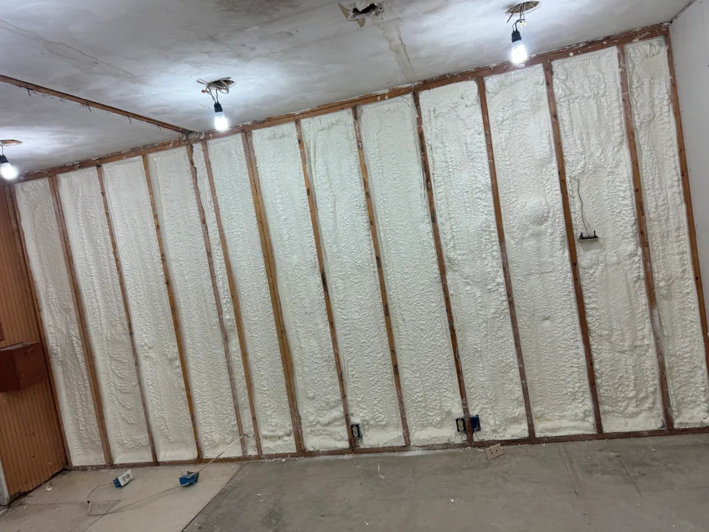 Foamed stud wall filling every bay in a room lit by two bare hanging bulbs