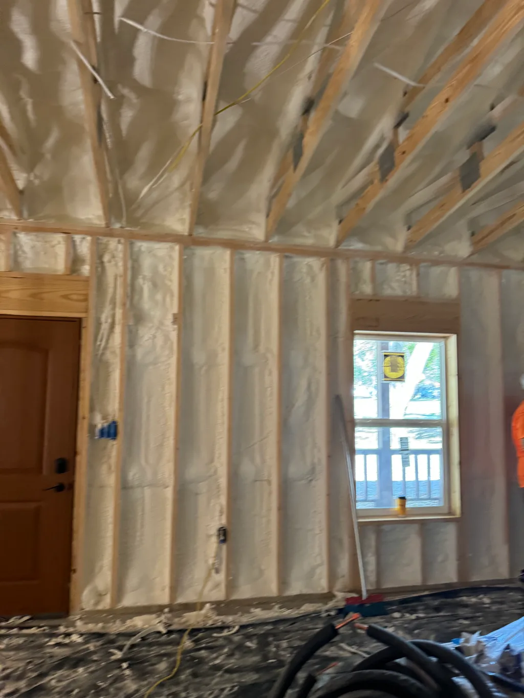 Foamed wall between a wooden door and a small window with hose coiled on the floor