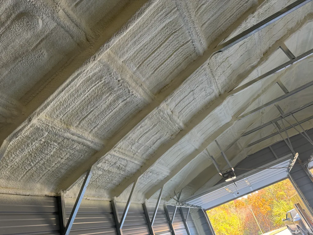 Foamed steel building roof with the end door rolled open onto autumn trees