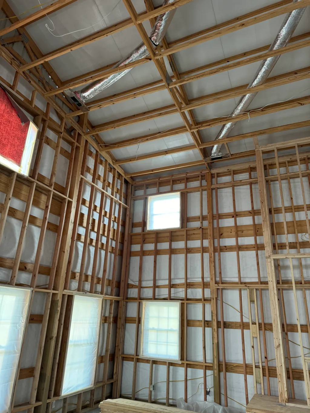 Pole barn framing with a foil duct overhead, windows and a red panel on the wall
