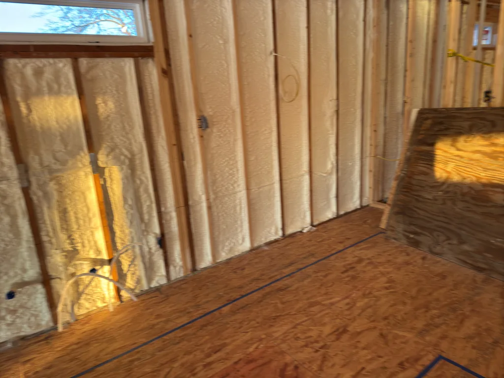 Warm evening light across a foamed stud wall above a bare plywood floor