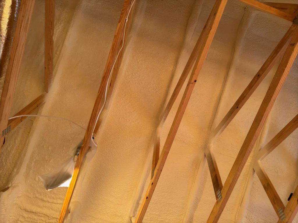 Rough foam across a ceiling between rafters, lit warm orange by low sunlight