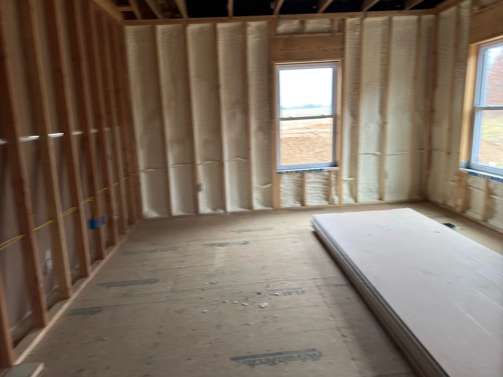 Corner of a foamed room with windows onto open fields and plywood sheets laid down
