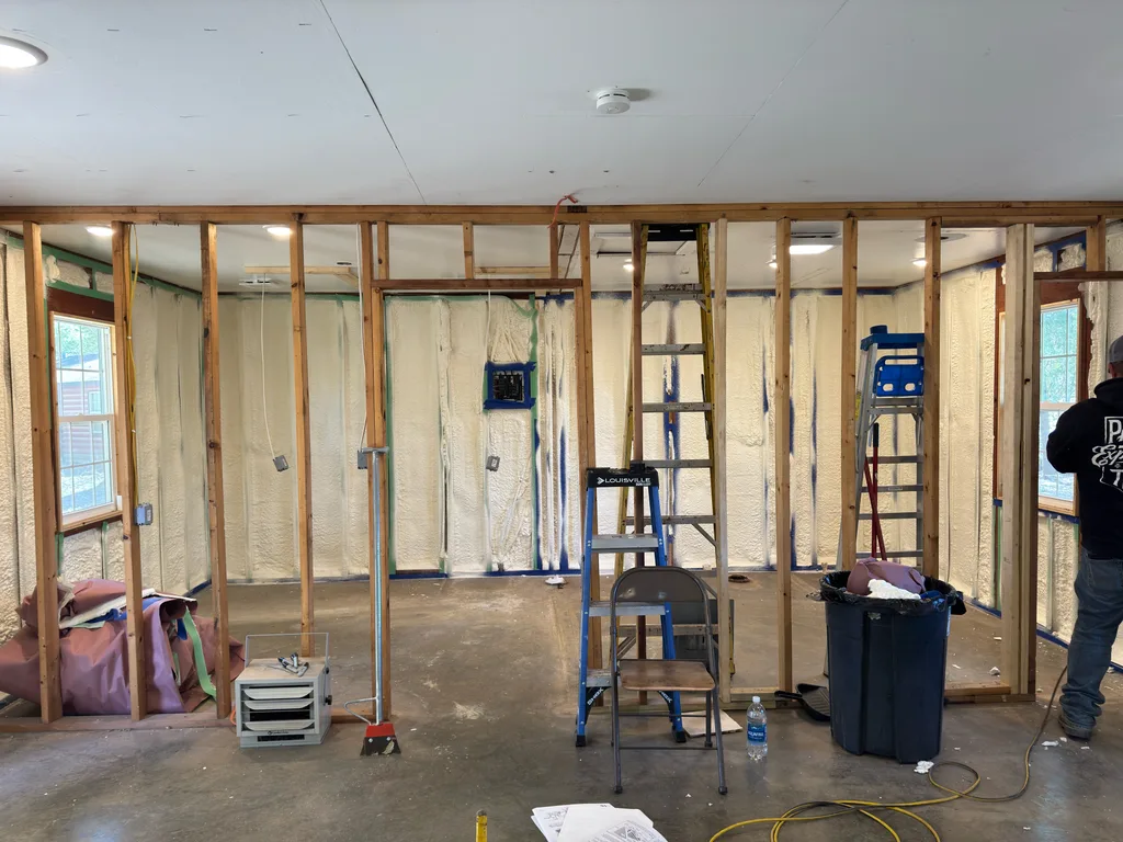 Room part way through insulating with bare studs, step ladders and two workers