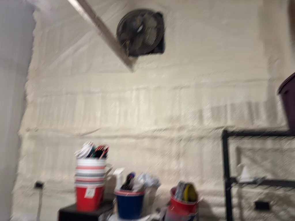 Foamed wall behind a mounted fan above a bench of buckets and supplies
