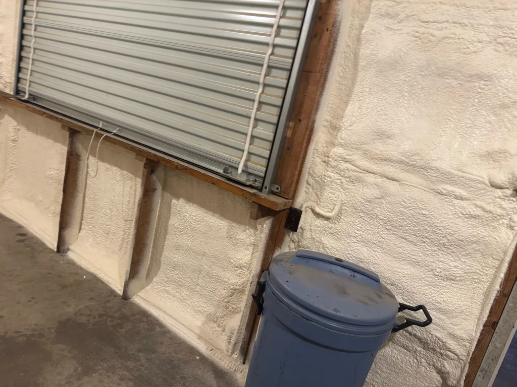 Foamed wall beside a rolled up steel door with a grey bin on the concrete floor