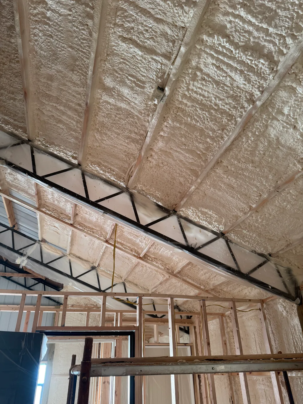 Foamed roof slope running down to black steel trusses in a tall open building